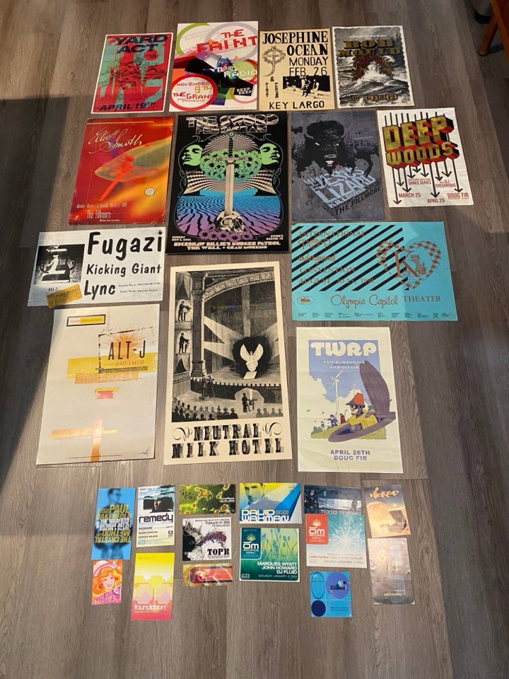 Gig posters laid out on a wood floor: Fugazi, Neutral Milk Hotel, The Sword, The Jesus Lizard, Elliott Smith, Bob Mould, TWRP, Alt-J, with a row of club flyers below.