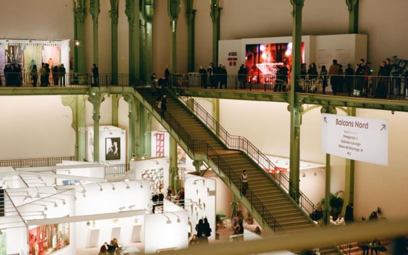 Art Basel Paris in the Grand Palais: fair booths below, visitors on the green iron balconies and staircase